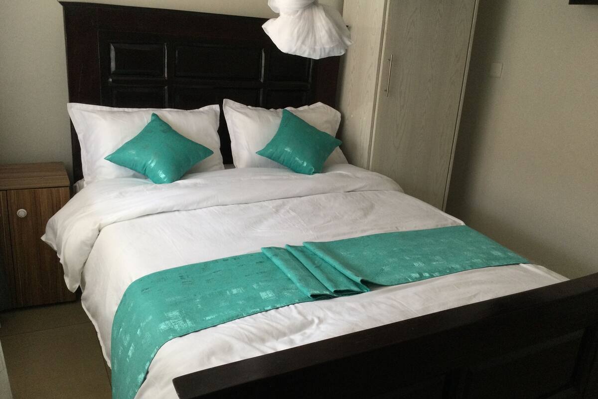 A bed with white bedding and teal pillows, a wooden headboard, and a teal throw blanket.