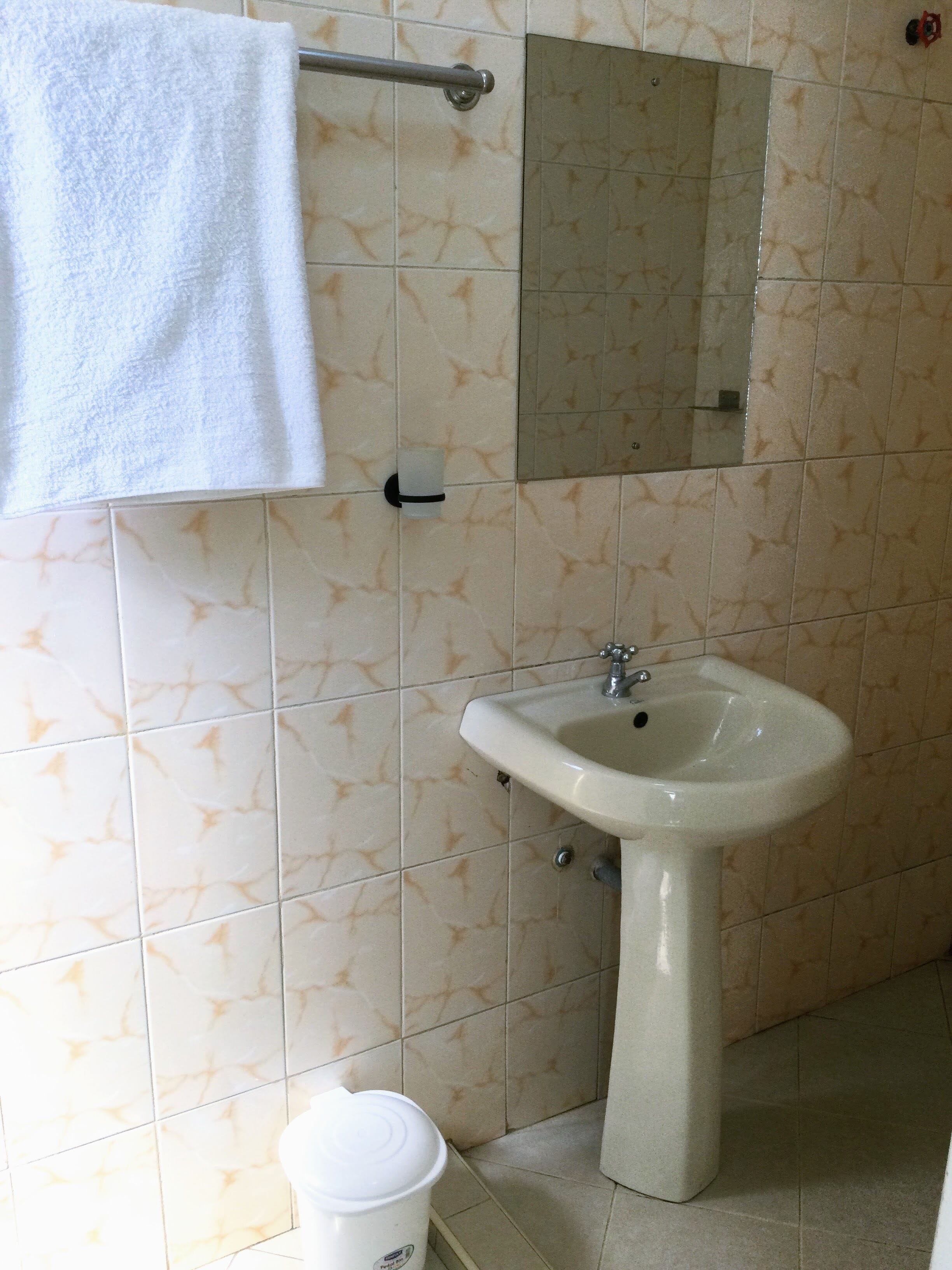 Une salle de bain avec un lavabo blanc, une serviette suspendue à un porte-serviettes et un miroir au-dessus du lavabo.