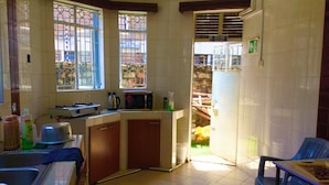 Una cocina con estufa a gas, microondas y un lavamanos. Hay ventanas con barrotes y vistas al exterior.