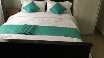 A neatly made bed with white bedding and teal pillows, a teal bedspread, and a dark wooden headboard.