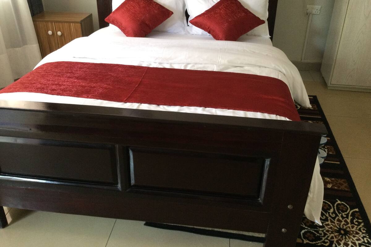 A bed with a dark wooden frame, white bedding, and two red pillows.