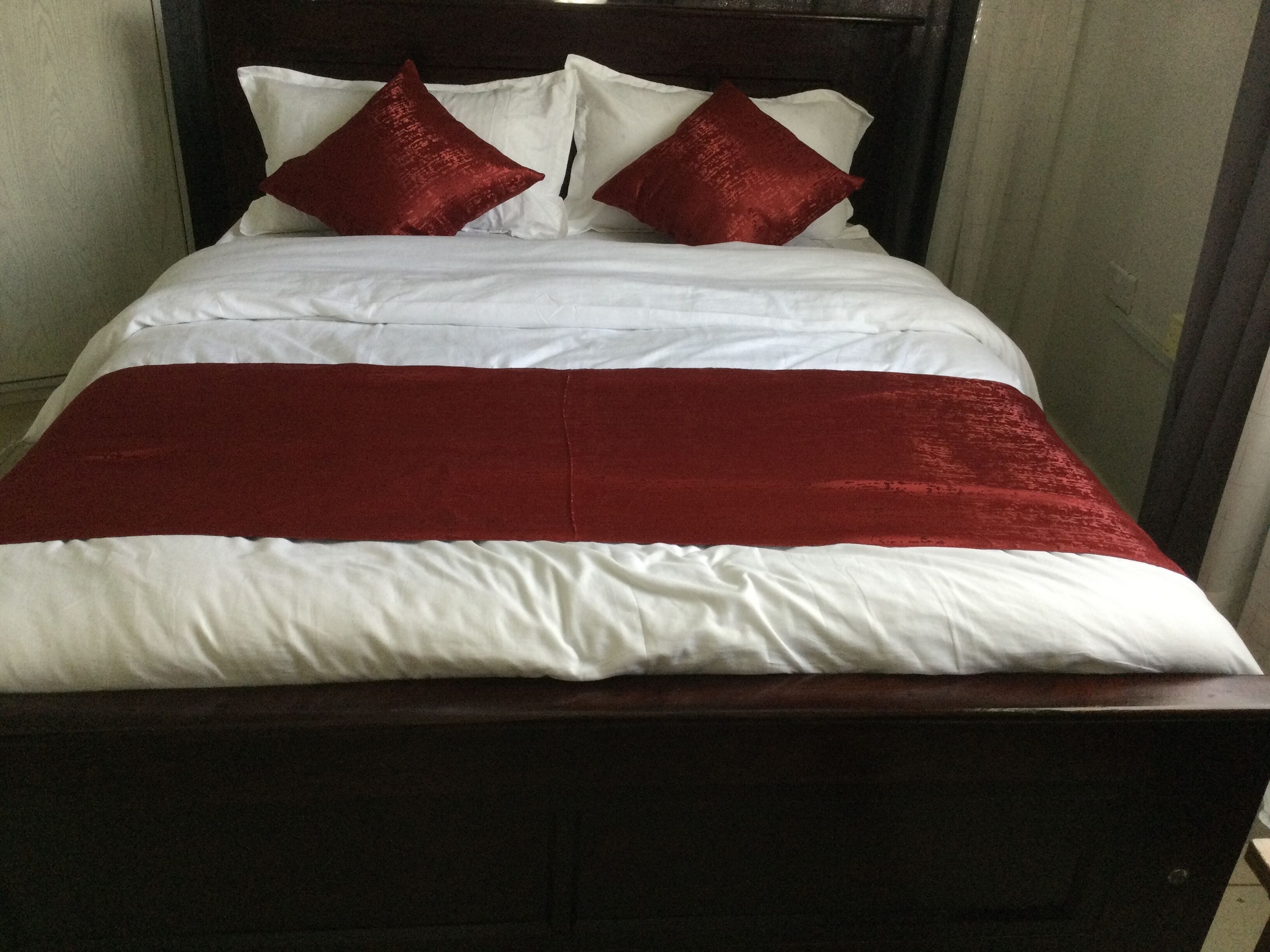 A bed with a wooden headboard, white and red bedding, and two red pillows.