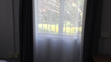 Una habitación de hotel con cama, ventana con cortinas y vista a un jardín.