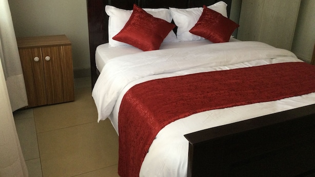 Una cama bien hecha con ropa de cama blanca y roja, una mesita de noche de madera y un cabecero oscuro.
