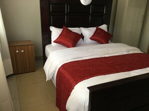 Una cama bien hecha con ropa de cama blanca y roja, una mesita de noche de madera y un cabecero oscuro.