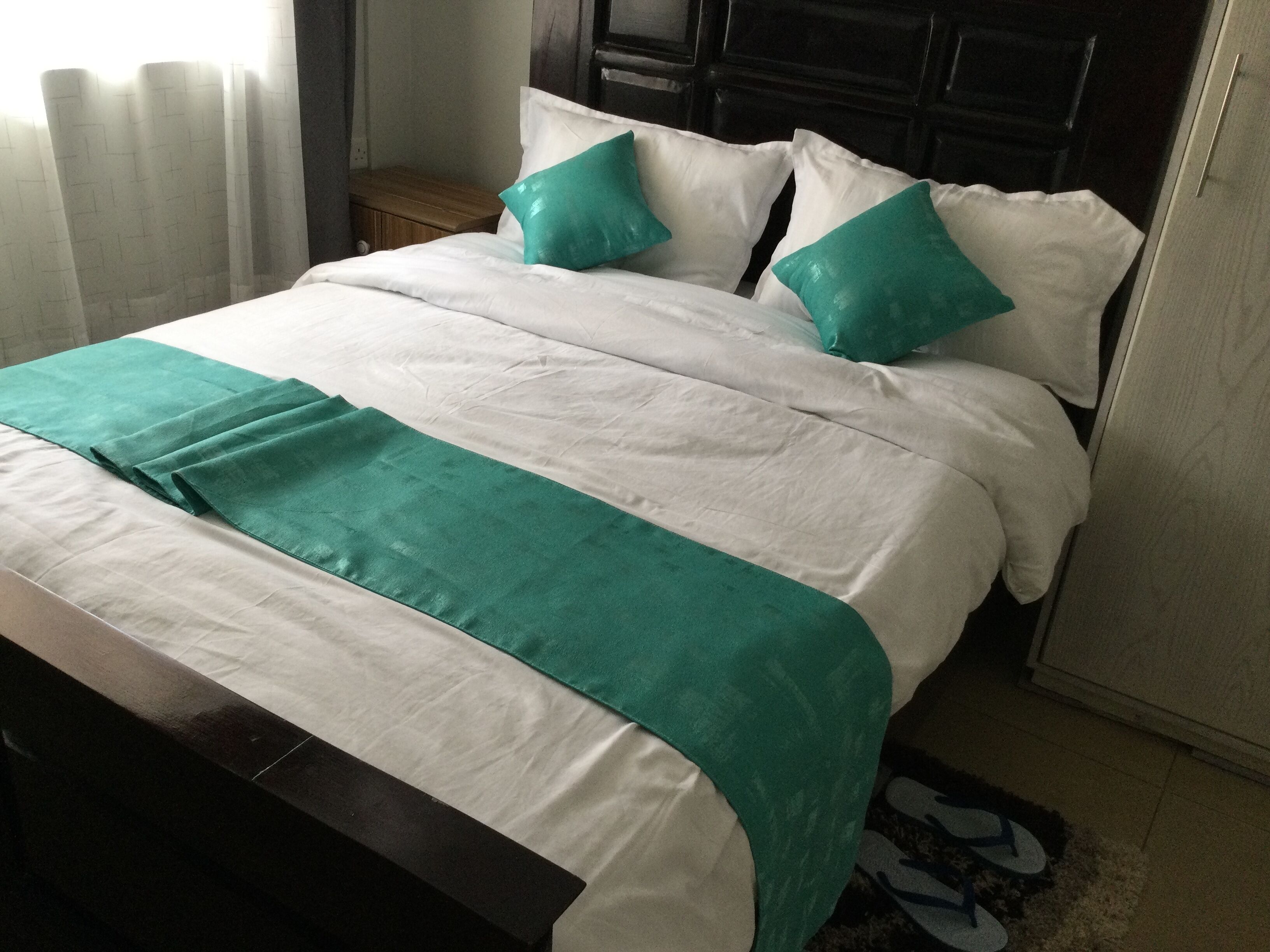A neatly made bed with white and teal bedding, a wooden headboard, and a wooden nightstand beside it.