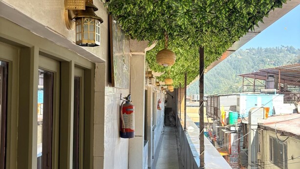 A narrow corridor with a green leafy canopy, a fire extinguisher, and a lantern on the wall. - HOTEL AMAR (Dehradun)