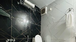 A bathroom with a toilet, a shower, and a sink. The floor has patterned tiles, and the walls are tiled with a mix of black and white tiles. - HOTEL AMAR (Dehradun)
