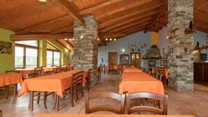 A restaurant with wooden beams and stone pillars, tables with orange tablecloths, and a stone fireplace. - Agriturismo il Runch (Viu)