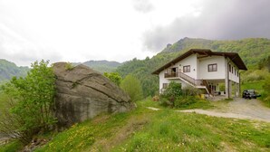 A two-story house with a balcony, surrounded by lush greenery and mountains. - Agriturismo il Runch (Viu)