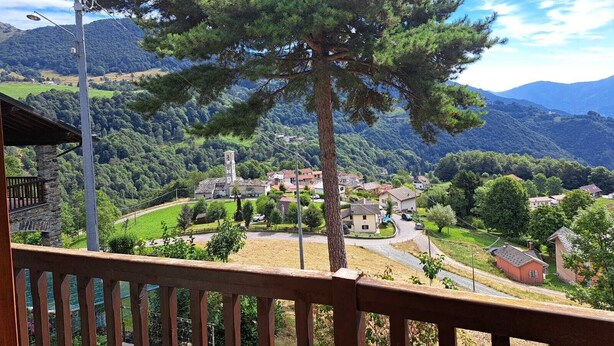 A balcony with a view of a village, a prominent pine tree, and a stone building with a clock tower. - Agriturismo il Runch (Viu)