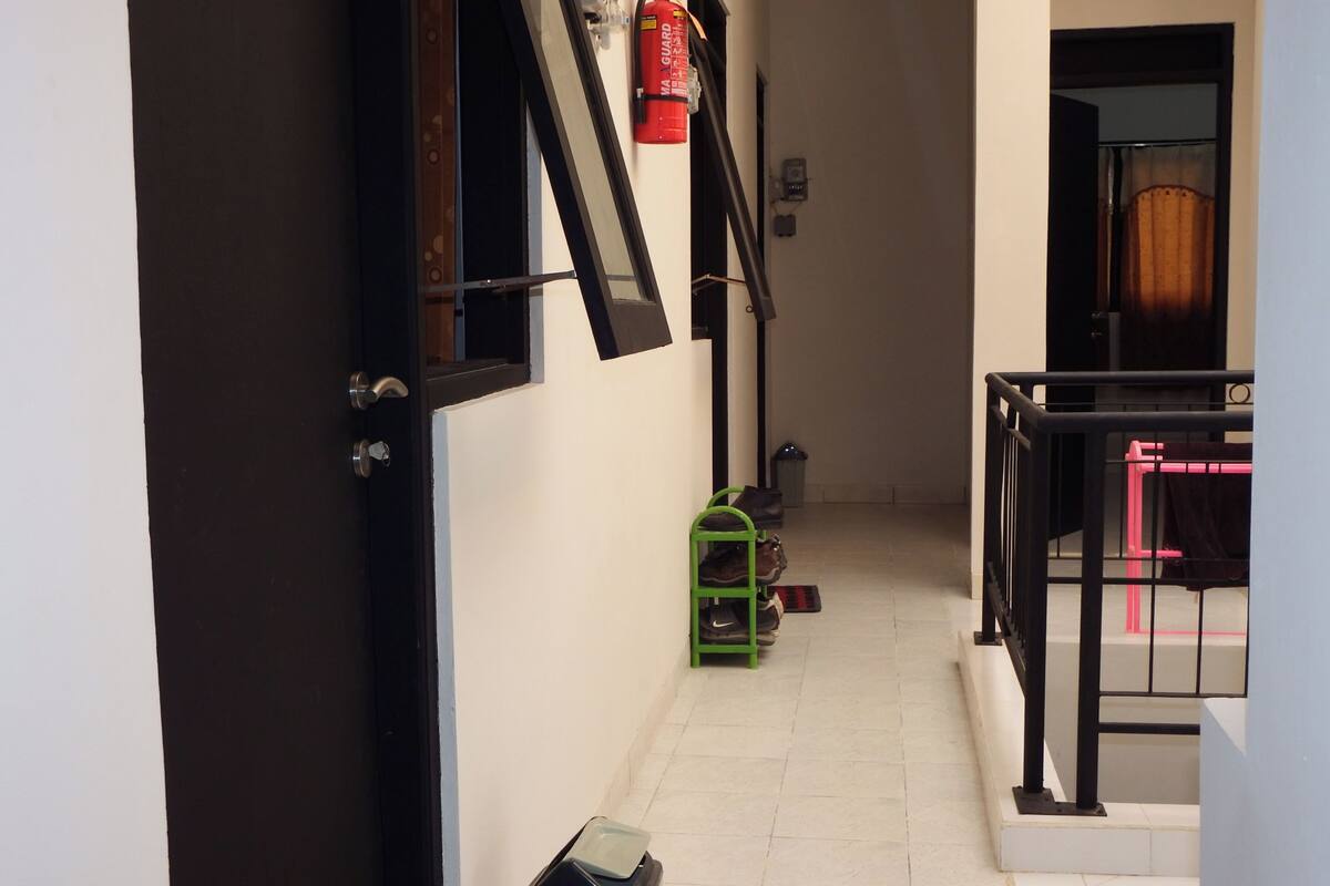 A narrow hallway with a fire extinguisher mounted on the wall, a trash bin, and a green shoe rack.