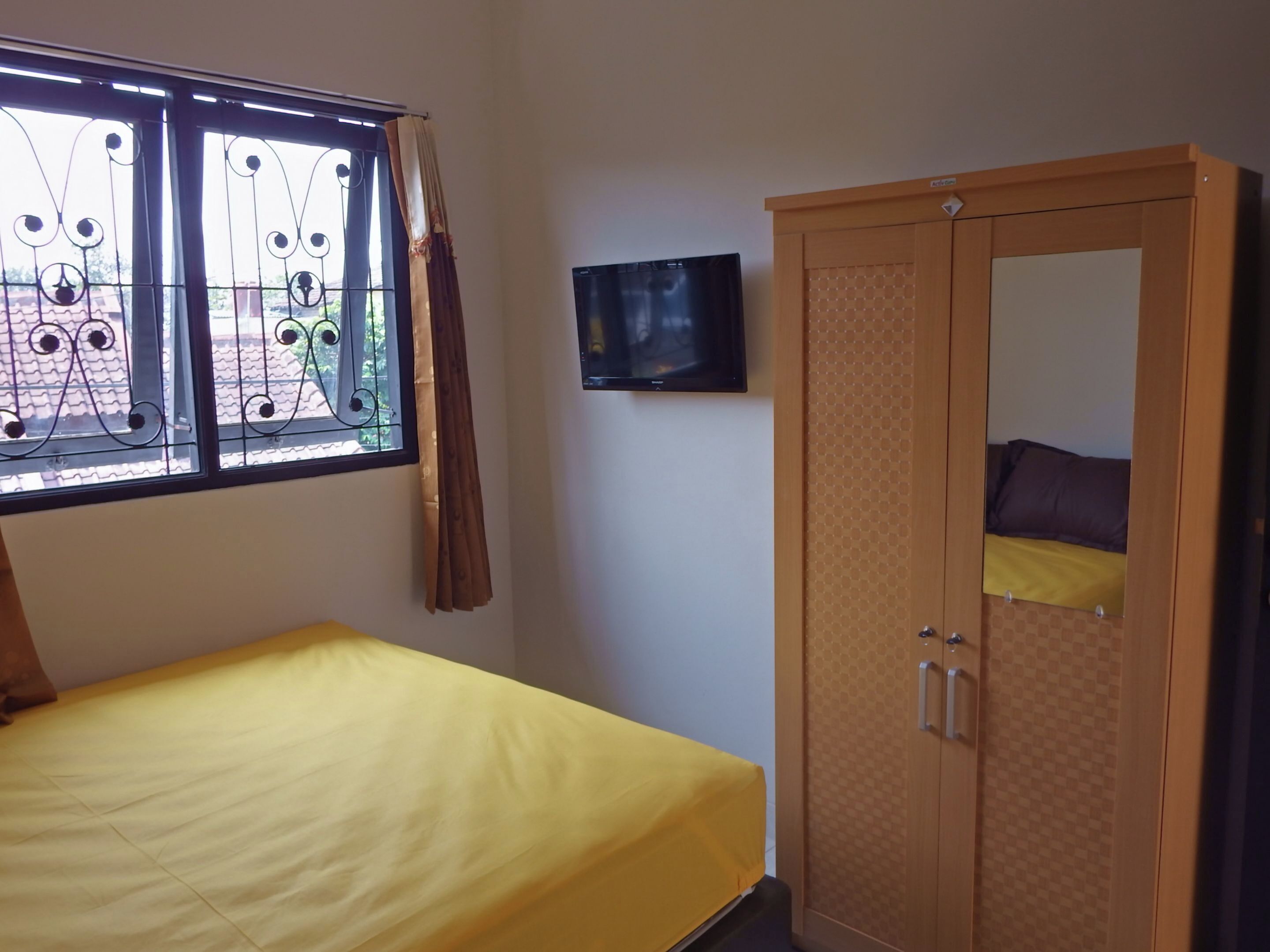 Una habitación con cama, armario, televisión y ventana con barrotes y cortinas.