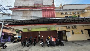 Un edificio con entrada cubierta, varias motocicletas estacionadas adelante y un letrero que indica un área de estacionamiento.