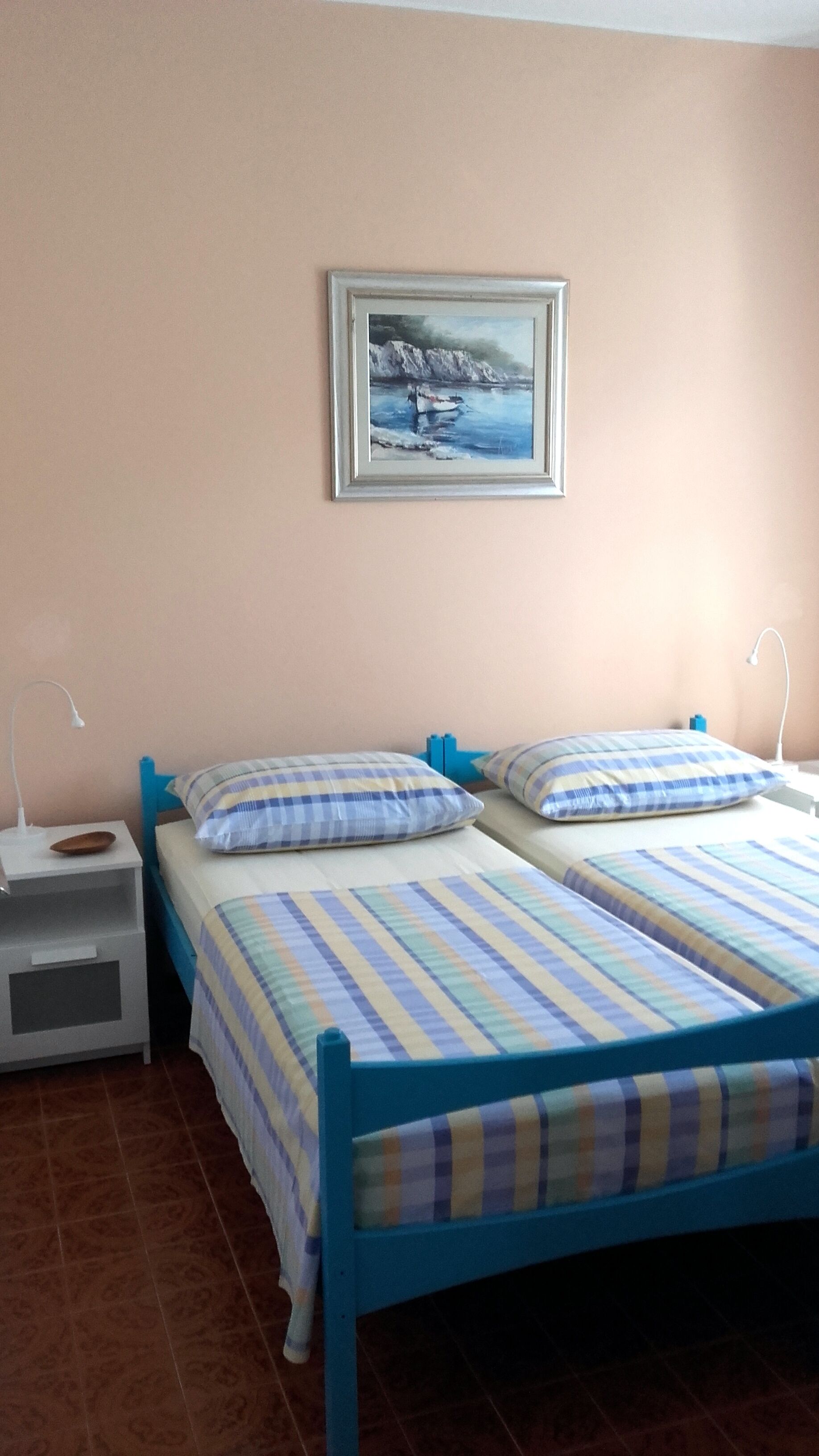 Une chambre avec deux lits, une table de chevet, une lampe et un tableau au mur.