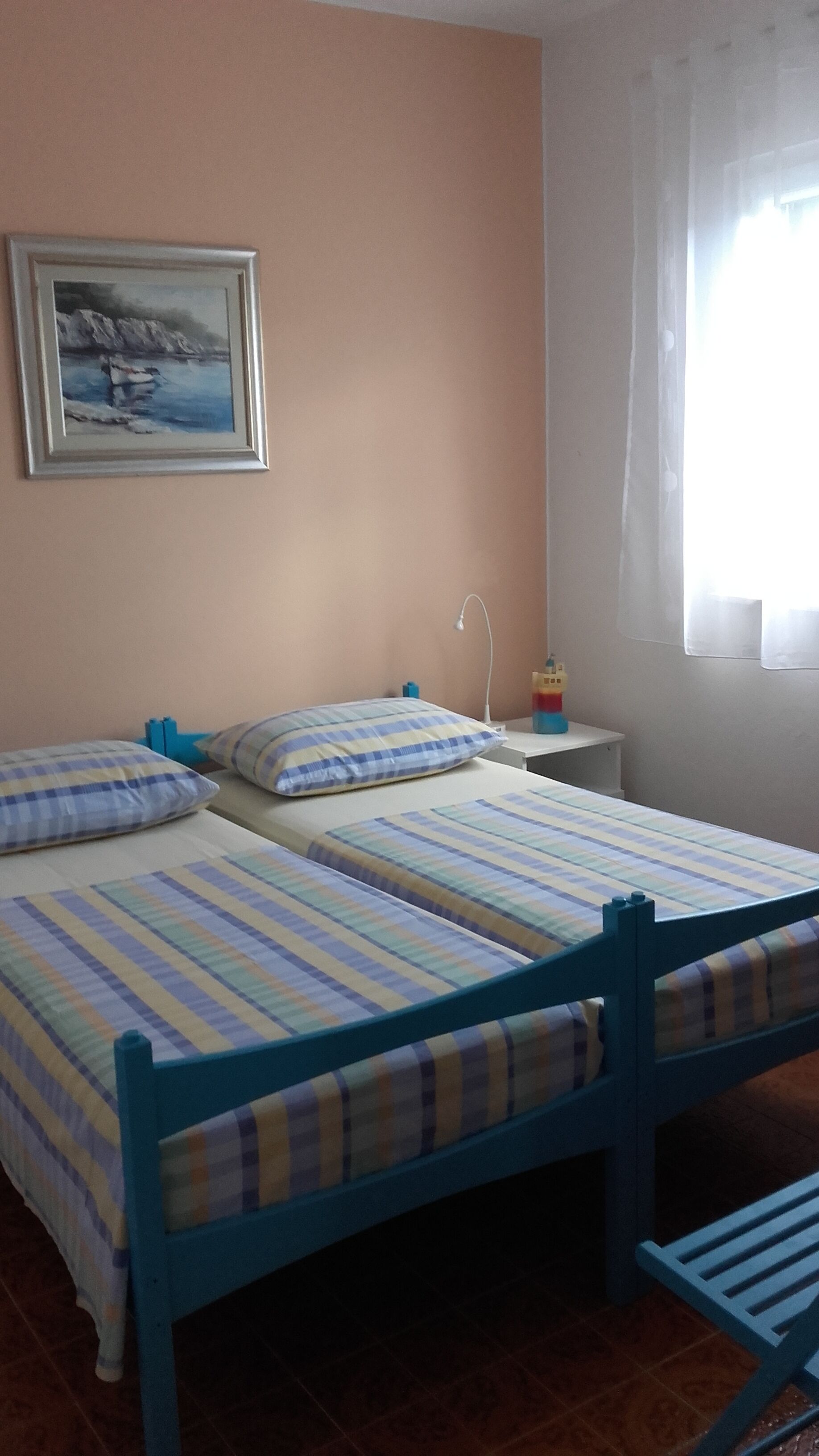 A room with two beds, a nightstand, a lamp, a painting, and a window with curtains.