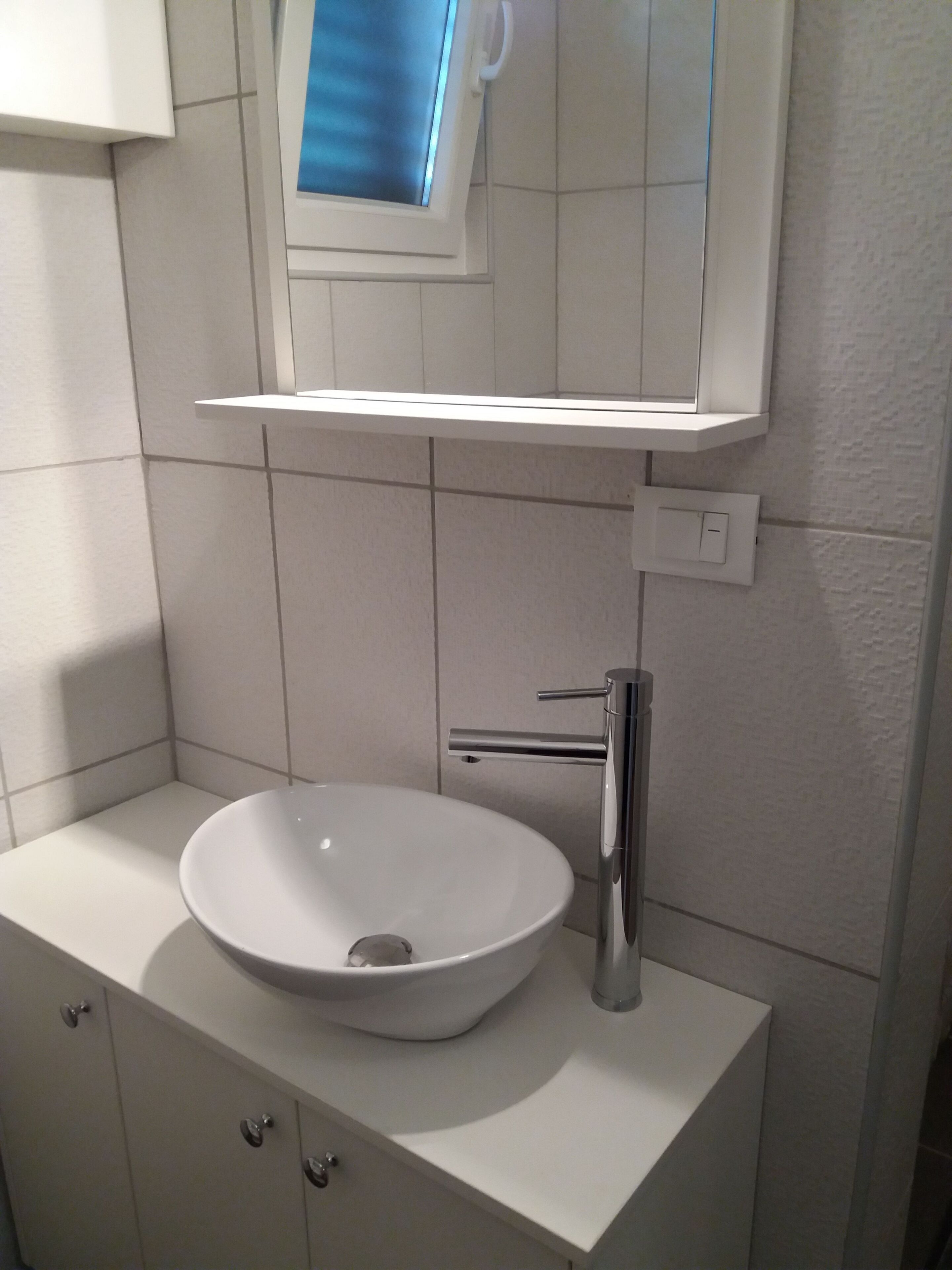 A bathroom with a white sink, a mirror, and a window above the mirror.