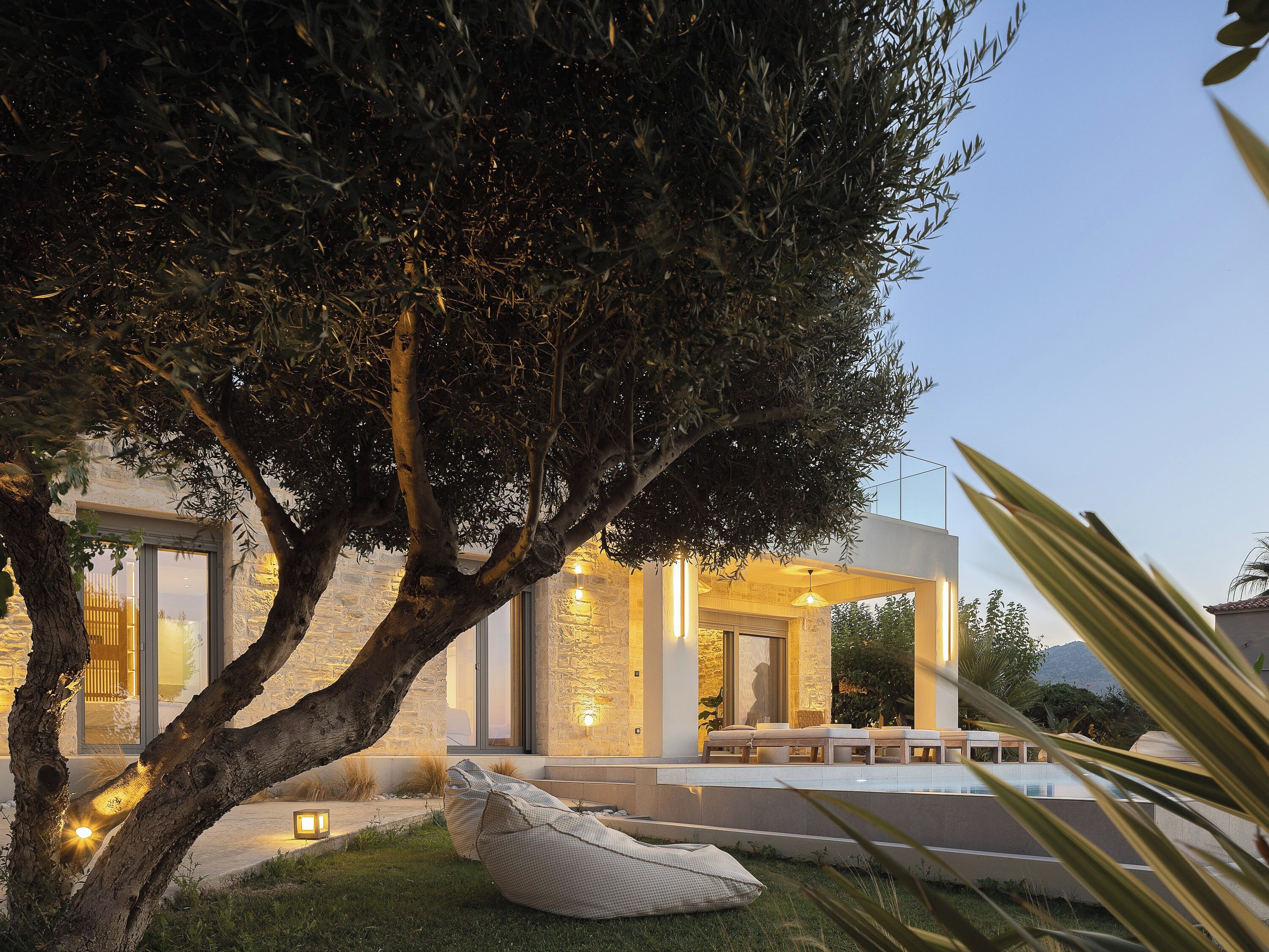 A modern outdoor seating area with a tree, a stone wall, and a pool.