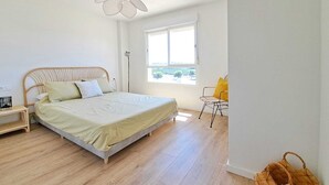 Ein Schlafzimmer mit Bett, Nachttisch, Stuhl, Fenster und einer Pendelleuchte.