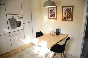Une cuisine de taille réduite avec une table en bois, des chaises noires et un luminaire suspendu.