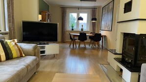 A modern living room with a flat-screen TV, a sofa, a dining table with chairs, and a fireplace.