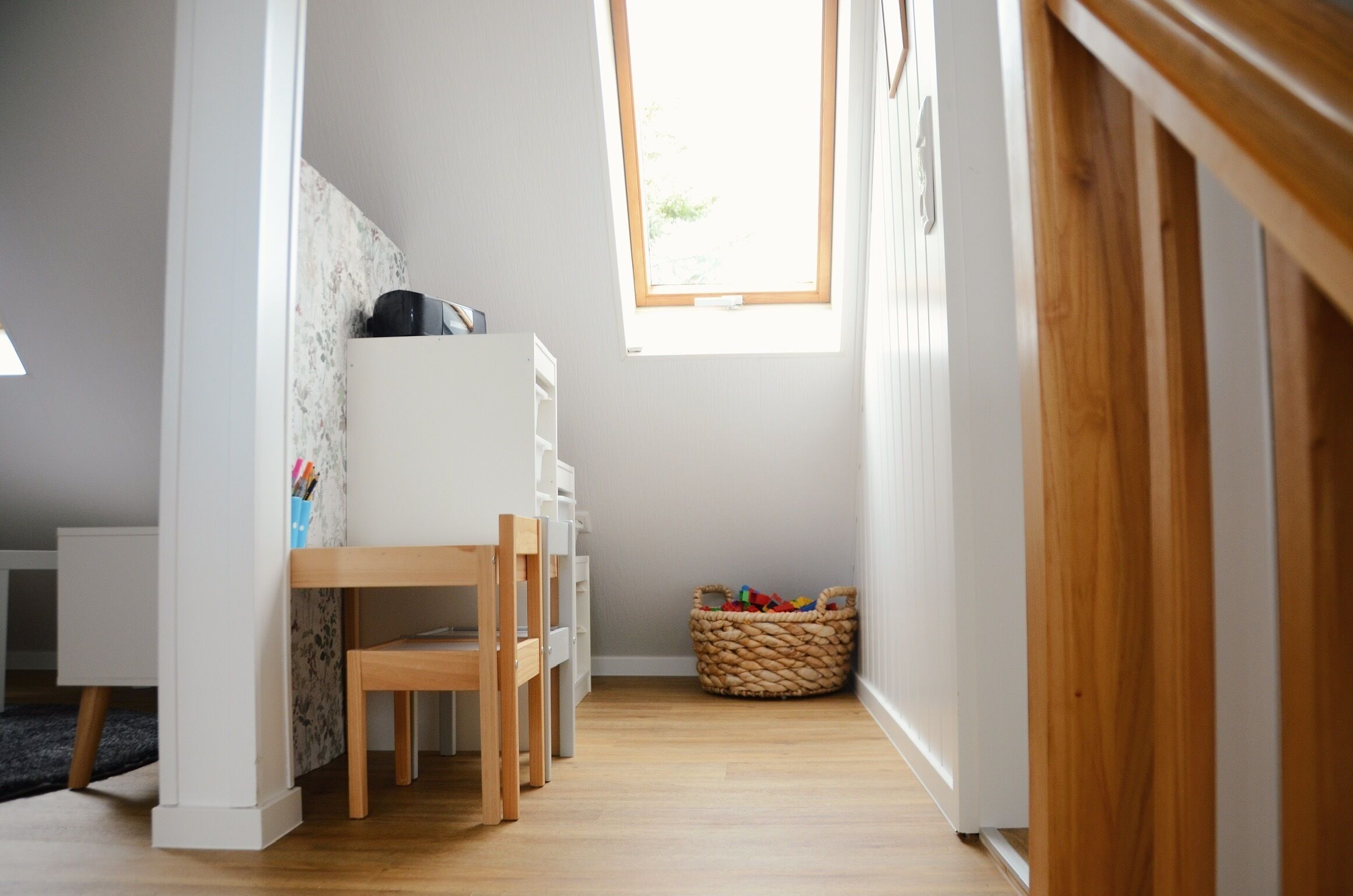 Une salle de jeux pour enfants avec un bureau en bois, des tiroirs et un panier rempli de jouets.