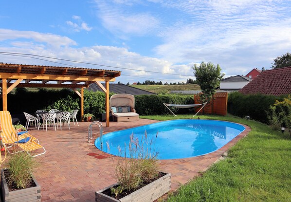 Un patio trasero con piscina, mobiliario de jardín y una pérgola.