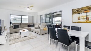 A modern living room with a sofa, coffee table, and dining area with chairs. - Relax Poolside by the Canal (BONGAREE)