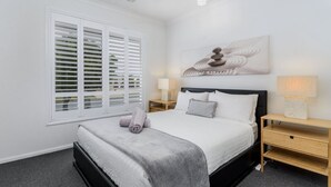 A bedroom with a bed, bedside tables, a window with blinds, and a wall-mounted artwork. - Relax Poolside by the Canal (BONGAREE)