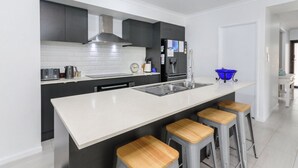 A modern kitchen with a central island, stainless steel appliances, and bar stools. - Relax Poolside by the Canal (BONGAREE)