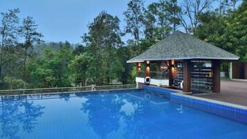A swimming pool with a gazebo and lounge area, surrounded by trees.