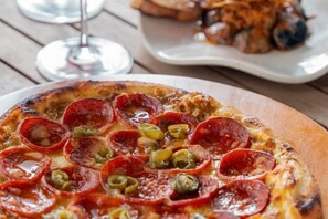 A pizza with pepperoni and jalapeños on a wooden table. - Coorg Marriott Resort & Spa (Kandanakolli)