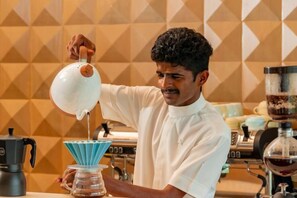 A person pouring liquid from a jug into a coffee maker. - Coorg Marriott Resort & Spa (Kandanakolli)