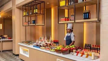 A buffet area with a variety of food items and beverages, a chef, and shelves with bottles.