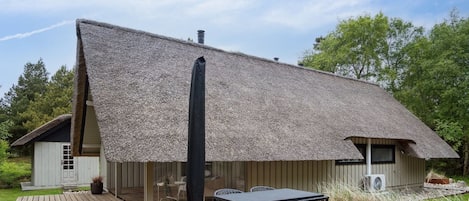 Ein Haus mit einem Strohdach, einer Holzterrasse und einem Tisch mit Stühlen.
