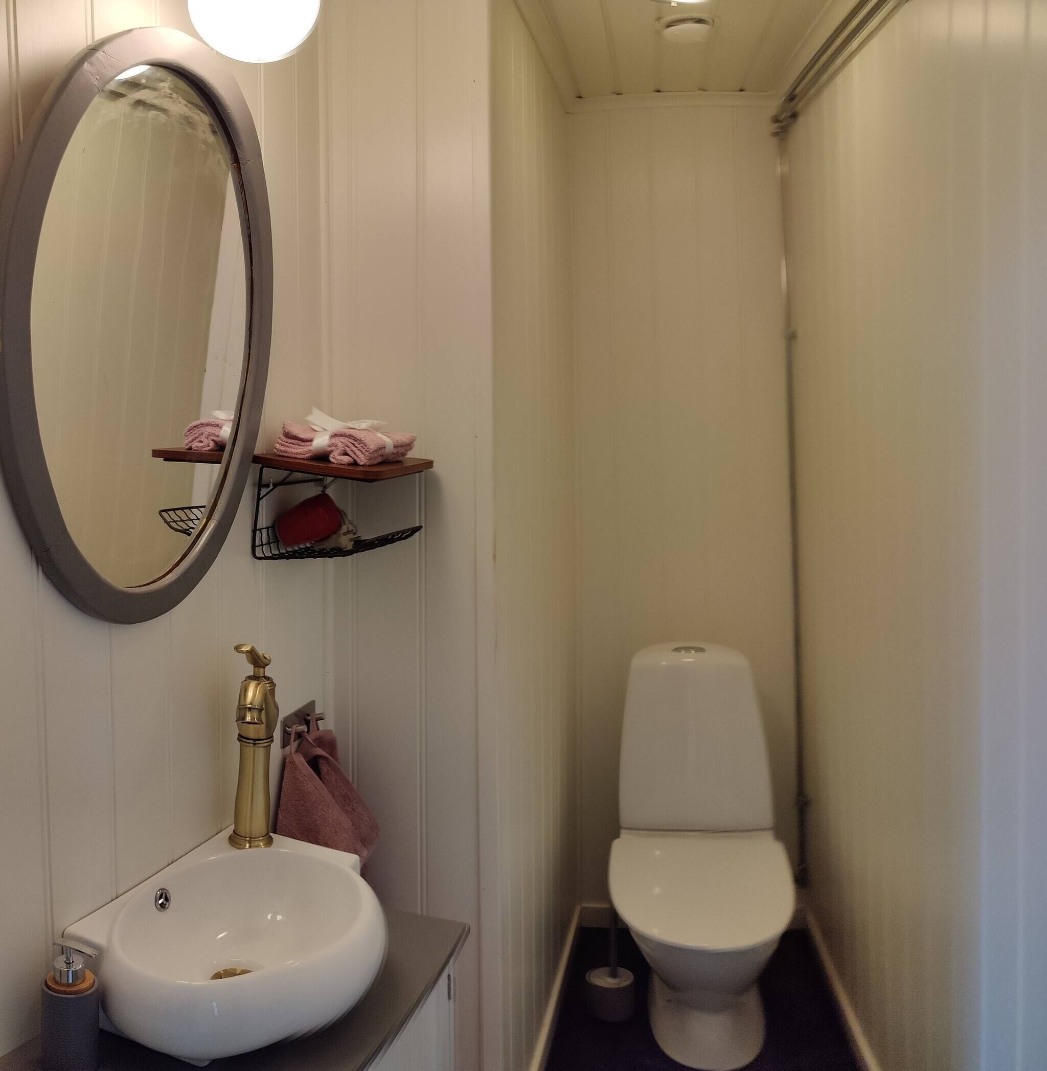 A bathroom with a white sink, a gold faucet, a mirror, a toilet, and a shelf with towels.