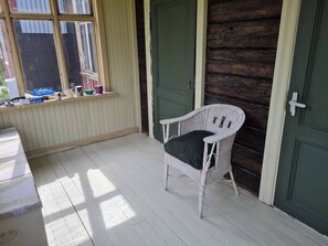 A room with a white wicker chair, a window with blinds, a green door, and a wooden floor.