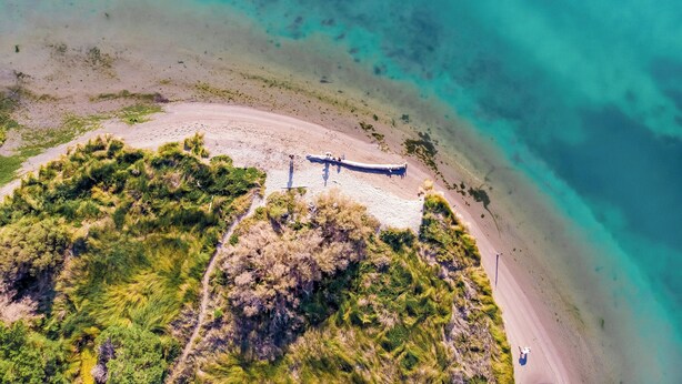 An aerial view of a beach with a boat on the shore, surrounded by vegetation and clear turquoise waters.