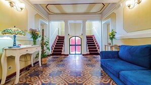 A spacious room with a blue sofa, a desk with a lamp, and a staircase leading to a door.