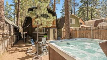 A hot tub in a backyard with a wooden deck, surrounded by trees and a house.