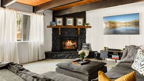 A cozy living room with a stone fireplace, a large window with curtains, a comfortable sofa, and a television. - Nily`s Squirrel Nest (Big Bear Lake)