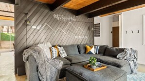 A modern living room with a sectional sofa, a coffee table, and a decorative wall with a zigzag pattern. - Nily`s Squirrel Nest (Big Bear Lake)