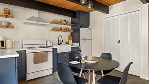 A compact kitchen with a stove, oven, and refrigerator, a dining table with chairs, and a wooden ceiling. - Nily`s Squirrel Nest (Big Bear Lake)