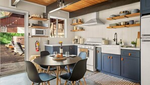 A modern kitchen with wooden beams, a dining area with a round table and chairs, and a view of the outdoors. - Nily`s Squirrel Nest (Big Bear Lake)