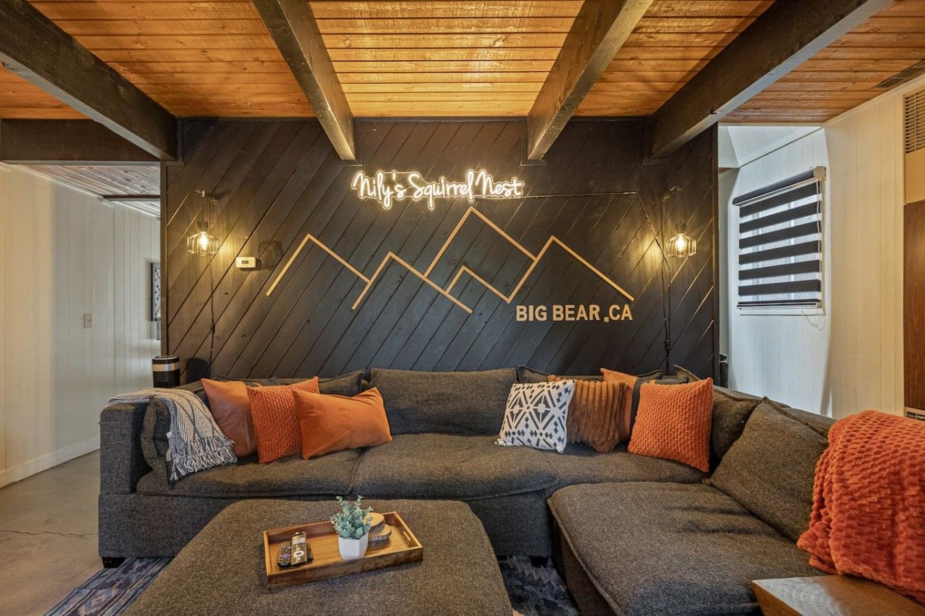 Un salon moderne avec un canapé d’angle, une table basse en bois et un néon mural.