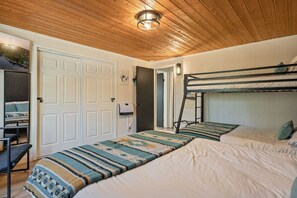 A room with a bunk bed, a desk with a chair, a white door, and a wall-mounted light fixture.