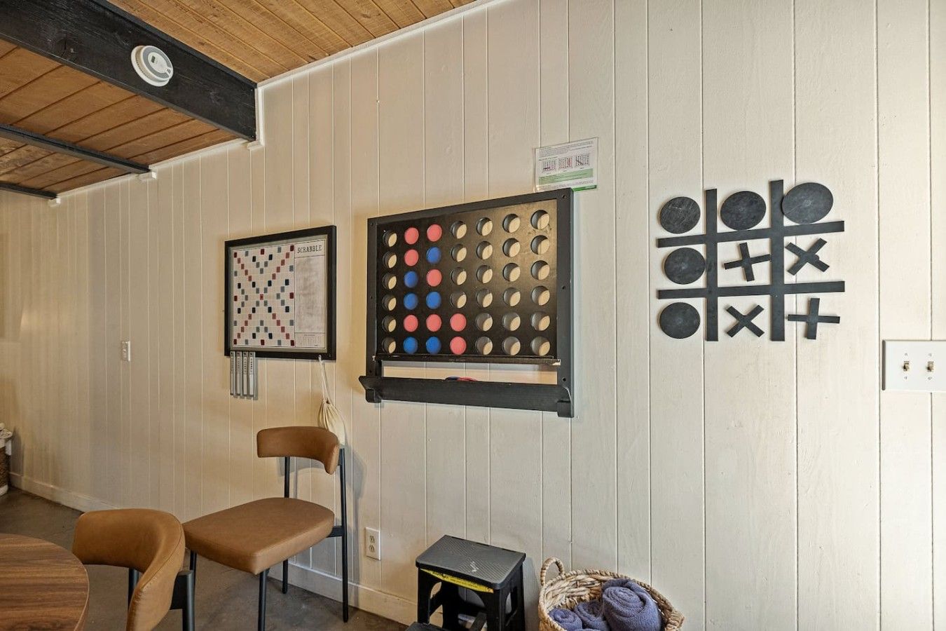 Quarto com um jogo de Scrabble, um jogo de batatinha quente e um tabuleiro emoldurado na parede. Há duas cadeiras e uma mesinha com uma cesta de toalhas.