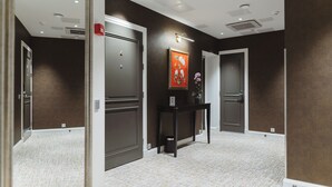 A hallway with dark walls, white trim, and a patterned carpet. There are doors on either side, a small table with a vase, and a framed picture on the wall. - Hotel Bastian  (Helsinki)
