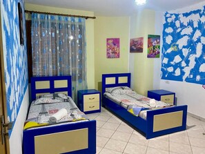 A room with two beds, a window with a curtain, and wall decorations.