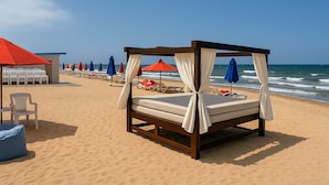 A beachside bed with a canopy, surrounded by beach chairs and umbrellas, with the ocean in the background. - Seaside Bliss Getaway (Al-Manasrah)
